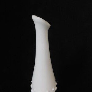 May include: White milk glass vase with a narrow neck and a bulbous base. The vase has a textured surface with small raised dots.