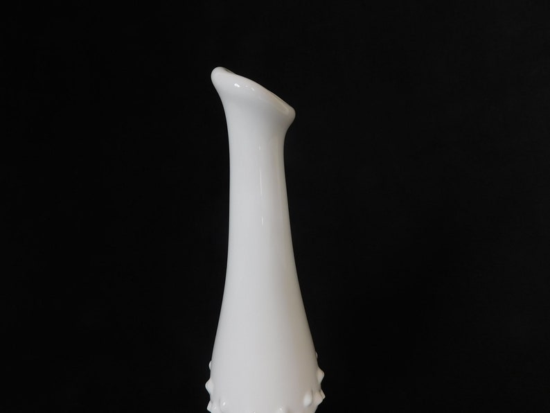 May include: White milk glass vase with a narrow neck and a bulbous base. The vase has a textured surface with small raised dots.
