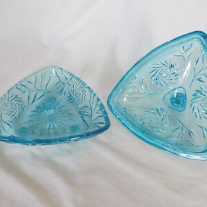 May include: A set of two vintage blue glass triangular dishes with a floral pattern. The dishes are made of clear glass with a light blue tint and have a delicate floral design etched into the surface. The dishes are perfect for serving snacks, desserts, or appetizers.