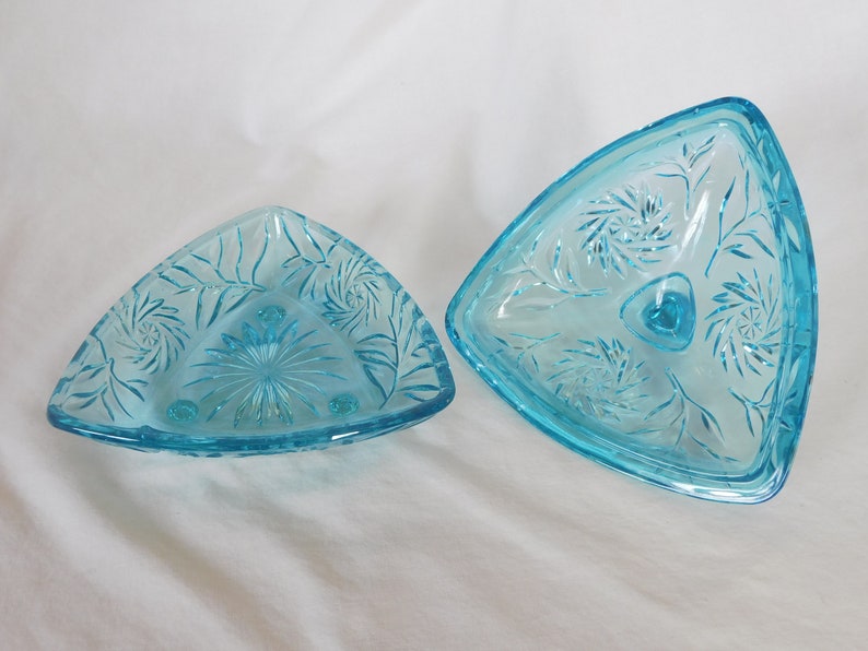 May include: A set of two vintage blue glass triangular dishes with a floral pattern. The dishes are made of clear glass with a light blue tint and have a delicate floral design etched into the surface. The dishes are perfect for serving snacks, desserts, or appetizers.