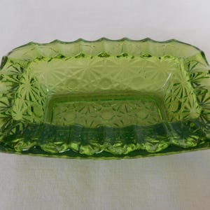 May include: A green glass ashtray with a square inner section and a scalloped edge.