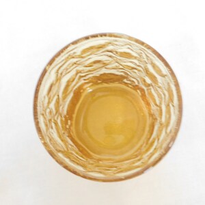 May include: A clear glass with a textured, rippled surface, filled with a light amber liquid.