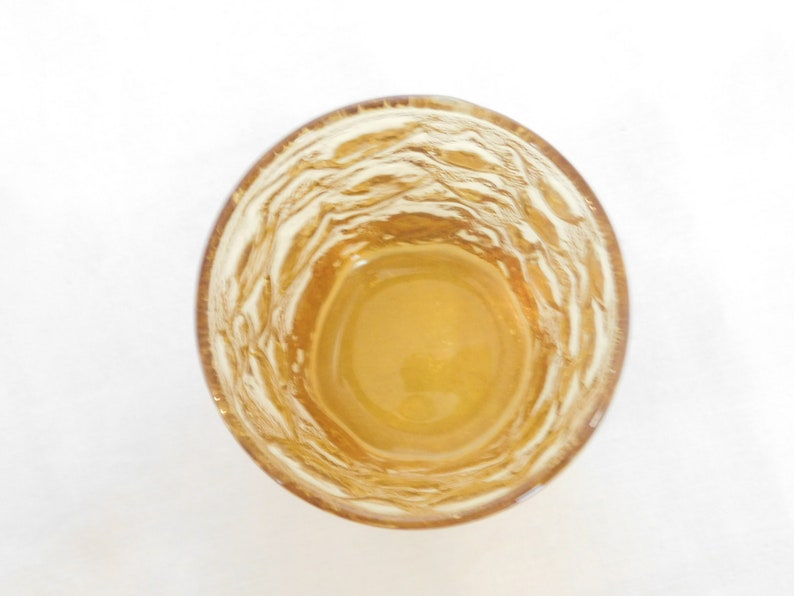 May include: A clear glass with a textured, rippled surface, filled with a light amber liquid.