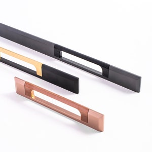 May include: A selection of contemporary cabinet handles in different metallic finishes. The handles are rectangular with a recessed grip and are in black, gold, and copper colours. The hardware is shown against a white backdrop.