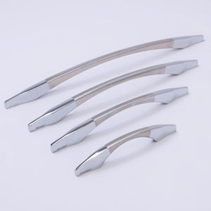 May include: Four cabinet handles in silver and brushed metal of different sizes are arranged diagonally. Each handle has a curved design with polished silver ends and a brushed metal centre. These handles are for furniture.
