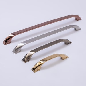 Peut inclure: Quatre poignées de meubles aux finitions métalliques variées : cuivre, argent, bronze et or. Chaque poignée présente un design incurvé avec une base géométrique. Les poignées sont disposées en diagonale, mettant en valeur leurs différentes tailles et finitions.