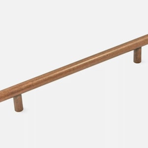 Könnte beinhalten: Ein kupferfarbener Schrankgriff mit einer zylindrischen Stange und zwei zylindrischen Pfosten. Die Hardware ist für eine einfache Installation konzipiert und verleiht jedem Schrank oder jeder Schublade eine warme Note. Der Griff ist etwa 30 cm lang.
