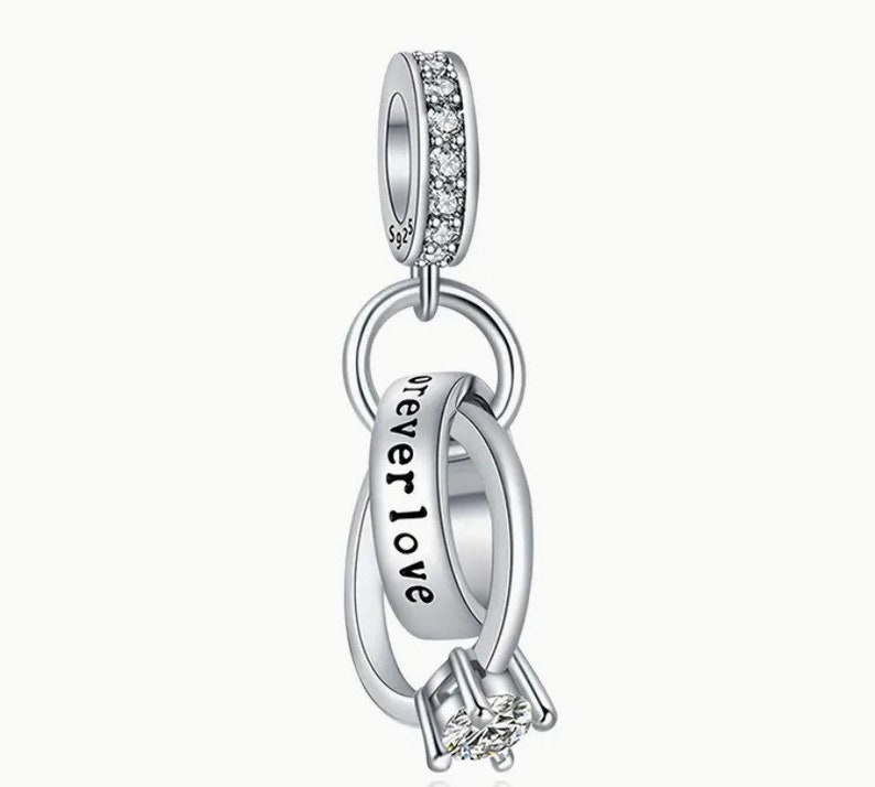 May include: Silver charm with two interlocking rings, one with the inscription "forever love". The rings are adorned with clear cubic zirconia stones.