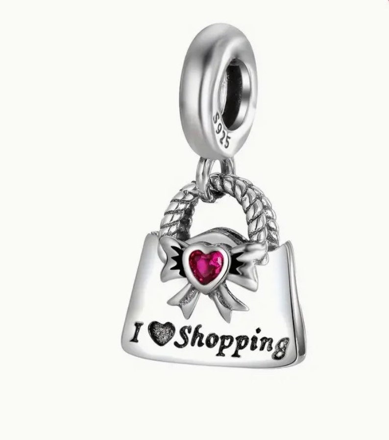 May include: Silver charm in the shape of a handbag with a red heart and the words "I love Shopping".