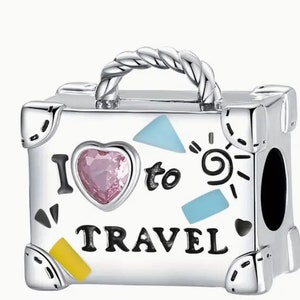 May include: Silver charm in the shape of a suitcase with a pink heart, blue and yellow accents, and the text "I love to travel".