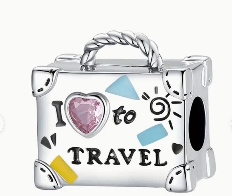 May include: Silver charm in the shape of a suitcase with a pink heart, blue and yellow accents, and the text "I love to travel".
