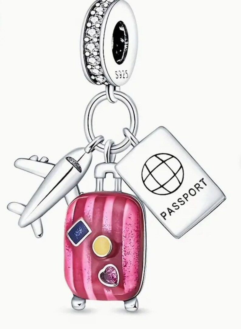 May include: Silver charm with a pink striped suitcase, a small airplane, and a passport with a globe on it. The charm has a silver loop for attaching to a bracelet or necklace.