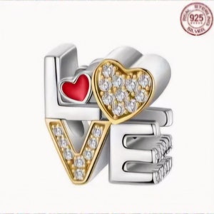 Op de afbeelding: Zilveren bedel met het woord "LOVE" gespeld in zilver en goud. De "O" is een rood hart met gouden rand en de "V" en "E" zijn versierd met heldere zirkonia-stenen.