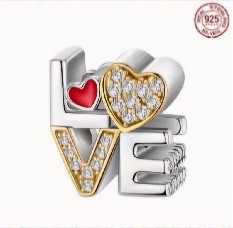 Op de afbeelding: Zilveren bedel met het woord "LOVE" gespeld in zilver en goud. De "O" is een rood hart met gouden rand en de "V" en "E" zijn versierd met heldere zirkonia-stenen.