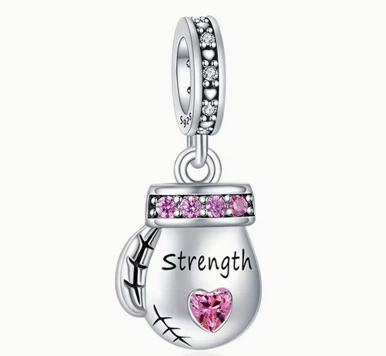 May include: Silver charm in the shape of a boxing glove with pink crystals and the word "Strength" inscribed on it. The charm has a heart-shaped crystal in the center.
