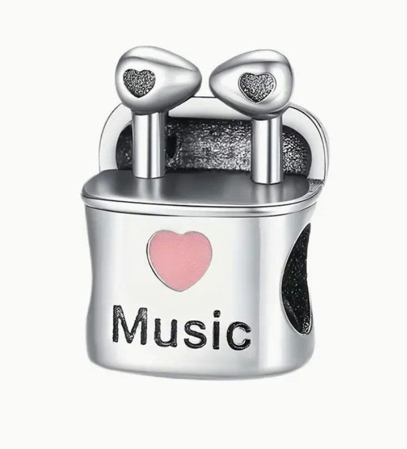 May include: Silver charm with a pink heart and the word "Music" on it. The charm features two silver earbuds with black hearts on them.