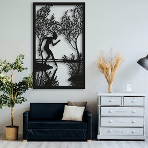May include: Black metal wall art featuring a silhouette of a person standing in a body of water with trees and foliage in the background.