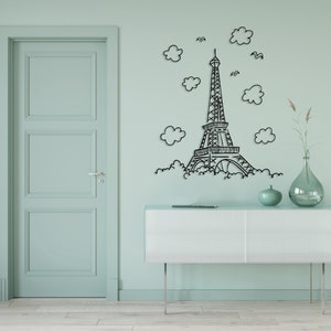 May include: A black metal wall decor featuring a stylized Eiffel Tower with clouds and birds. The decor is mounted on a light green wall above a white dresser.