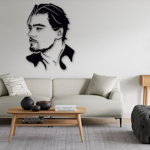 Puede incluir: Arte mural de silueta negra del perfil de un hombre. La habitación cuenta con un sofá de color claro, mesas de madera y un otomano gris. Jarrones negros decorativos y libros están en la mesa de centro. La habitación tiene un diseño moderno y minimalista.