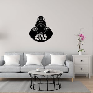 May include: A black and white wall clock featuring Darth Vader from Star Wars. The clock is shaped like a vinyl record and has the words "Star Wars" printed below the image.