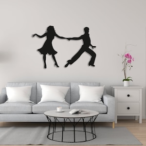Peut inclure: Décoration murale en silhouette noire d'un couple dansant. La silhouette est montée sur un mur blanc dans un salon avec un canapé, une table basse et une table d'appoint avec une plante.
