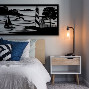May include: Black metal wall art depicting a sailboat on the water with a lighthouse and trees in the background.