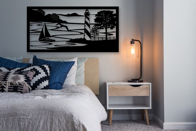 May include: Black metal wall art depicting a sailboat on the water with a lighthouse and trees in the background.