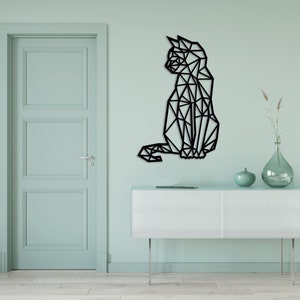 Peut inclure: Une décoration murale en forme de silhouette de chat géométrique noire sur un mur vert clair avec une commode blanche et un vase avec des fleurs séchées.