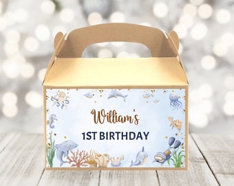 May include: A brown cardboard favor box with a handle, decorated with an underwater theme. The box features illustrations of sea creatures like dolphins, seahorses, and a narwhal, with the text "William's 1st Birthday".