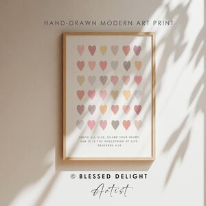 May include: A framed art print featuring a grid of small, multi-colored hearts in shades of pink, yellow, and grey. Below the hearts, the text reads: Above all else, guard your heart, for it is the wellspring of life. Proverbs 4:23.