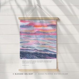 Peut inclure: Une impression aquarelle peinte à la main représentant un coucher de soleil sur l'océan. L'œuvre d'art présente des nuances de rose, d'orange et de bleu. Le texte "DECLARE HIS GLORY AMONG THE NATIONS..." est inclus.