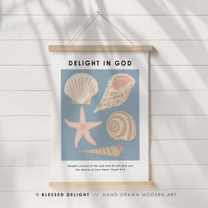 May include: A framed print featuring a blue background with illustrations of seashells and a starfish in shades of pink and beige. The text "DELIGHT IN GOD" is at the top, with a Bible verse below. The bottom reads "BLESSED DELIGHT // HAND-DRAWN MODERN ART."