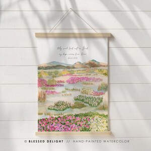 Peut inclure: Impression d'art aquarelle repr&eacute;sentant un paysage avec des fleurs roses et jaunes et une cha&icirc;ne de montagnes. Le texte dit : &laquo; Mon &acirc;me, trouve le repos en Dieu, mon espoir vient de Lui. Psaume 62:5. &raquo; L'&oelig;uvre est affich&eacute;e sur un support en bois.