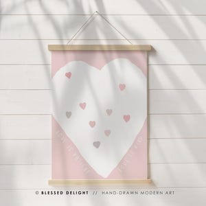 Peut inclure: Une affiche rose et blanche avec un motif de cœur. Le cœur est blanc avec de petits cœurs roses et gris éparpillés. Les mots "Love is Patient" et "Love is Kind" sont écrits sur les côtés.