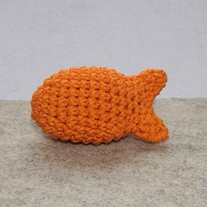 May include: A crocheted orange fish toy. The fish is made with a soft, textured yarn and has a slightly curved shape.