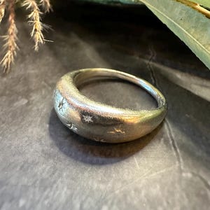 May include: A silver ring with a rounded, smooth surface and a design of small stars.