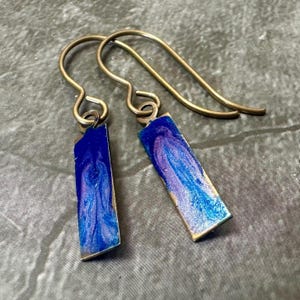 Könnte beinhalten: Ein Paar Ohrringe mit blauen und violetten, marmorierten, rechteckigen Anhängern aus Metall und goldfarbenen Haken.