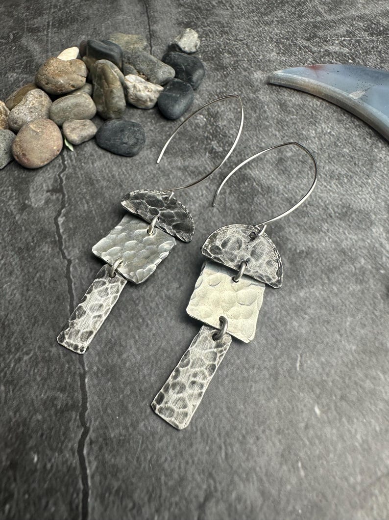 May include: A pair of silver earrings with a hammered texture. Each earring features a half-circle top, a square middle, and a rectangular bottom, all connected by small loops. The earrings have a dark, oxidized finish and dangle from thin, curved ear wires.