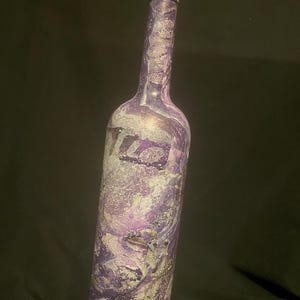 May include: A purple glass bottle with a marbled design and gold accents. The bottle is painted with a swirling pattern of purple, white, and gold.