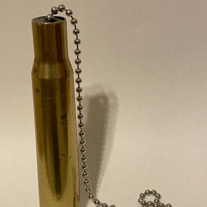 May include: A brass-colored bullet casing with a silver ball chain attached. The casing is cylindrical with a rounded base and a slightly tapered neck. The chain is connected at the top.