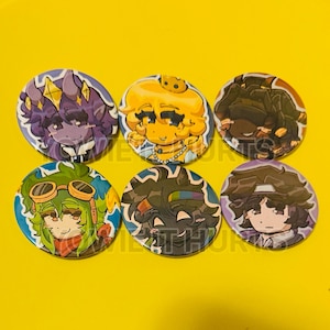 May include: Six circular pin-back buttons featuring colorful anime-style character illustrations. The designs include a purple horned figure, a yellow character with a crown, a dark-haired figure, a green-haired character with goggles, a dark-haired figure with a rainbow headband, and a brown-haired character.