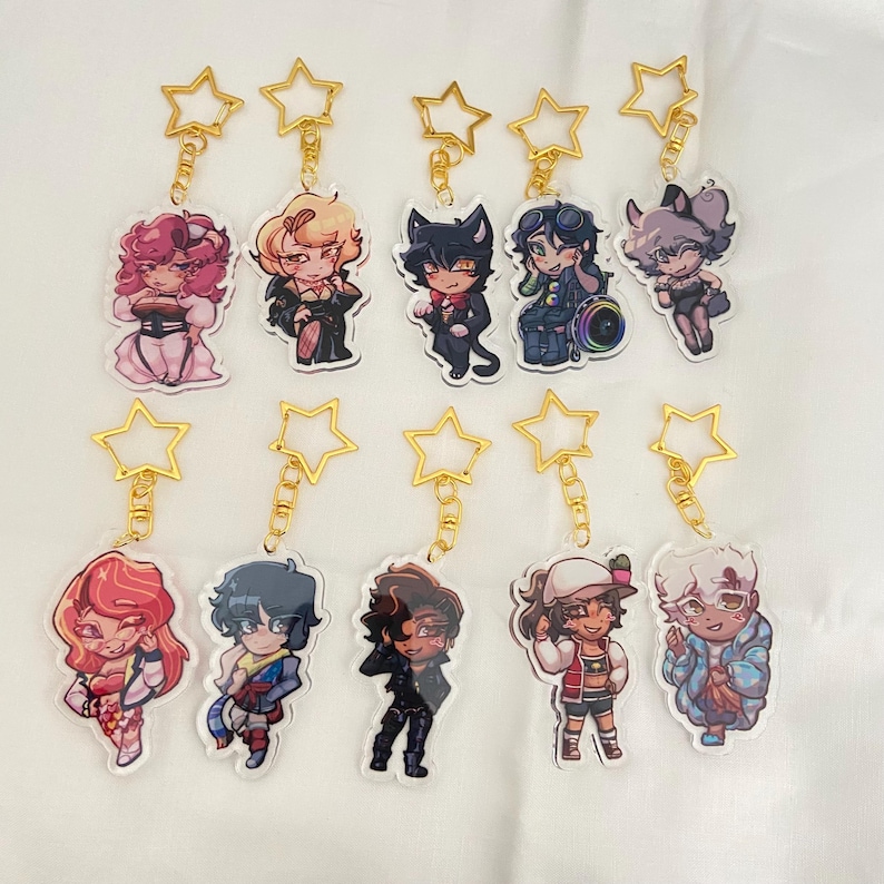 K&ouml;nnte beinhalten: Sammlung von Acryl-Schl&uuml;sselanh&auml;ngern mit verschiedenen Charakteren im Anime-Stil. Jeder Schl&uuml;sselanh&auml;nger hat einen goldenen sternf&ouml;rmigen Verschluss. Die Charaktere sind in farbenfrohen Outfits und Posen dargestellt, mit unterschiedlichen Frisuren und Gesichtsausdr&uuml;cken.
