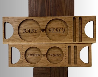 Peut inclure: Plateau de service en bois avec des noms gravés et des symboles de cœur. Le plateau comporte deux découpes circulaires pour les verres et une poignée. Les noms "BABE" et "BEBLY" sont gravés sur le plateau supérieur, et "JORDAN" et "TAYLOR" sur le bas.