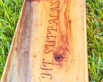 Peut inclure: Un plateau de service rectangulaire en bois avec le texte gravé "THE SUPPALAS". Le plateau présente un motif de grain de bois naturel avec des variations de couleur du brun clair au brun foncé. Le plateau est sur de l'herbe verte.
