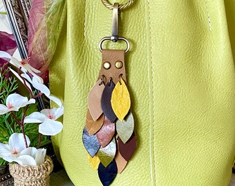May include: A green leather tote bag with a leather tassel keychain. The tassel is made of multiple leather leaves in various colors, including brown, yellow, and green.