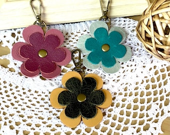 May include: Three leather flower keychains with metal rings. The flowers are layered and have a textured look. The colors are pink, teal, and brown.