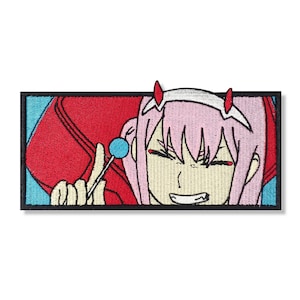 Może przedstawiać: Naszywka haftowana przedstawiająca postać anime z różowymi włosami, czerwonymi rogami i przebiegłym uśmiechem, trzymającą niebieską lizak. Postać jest ubrana w czerwono-niebieski strój.