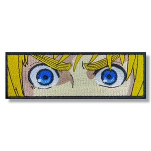 May include: Close-up of a pair of blue eyes with yellow hair, embroidered on a patch.