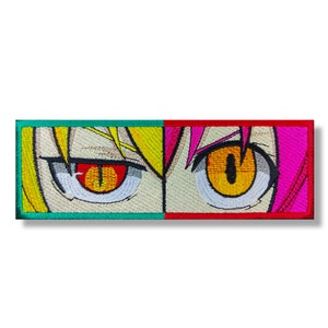 May include: A close-up of two anime eyes with yellow and red irises. The eyes are embroidered on a patch with a green and red border.