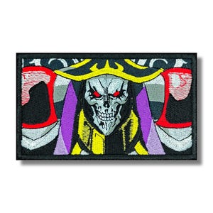 May include: Embroidered patch featuring a skeletal figure with red eyes, wearing a yellow and black robe, a purple cape, and a gold crown. The patch has a black border and is rectangular in shape. The design is detailed and colorful.